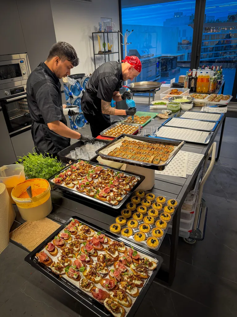Two chefs plating trays of canapés and tartlets on a long prep table